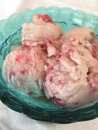 Scoops of strawberry ice cream in a teal glass bowl on a white tablecloth.