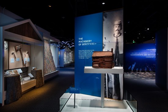 A view of an exhibit. Much of it is dark but some of it is spot-lit. There are signs and artifacts on pedestals.