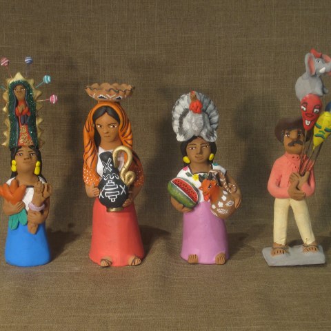 Four figurines lined up against a background. They wear colorful clothing, carry different items and have objects on their heads